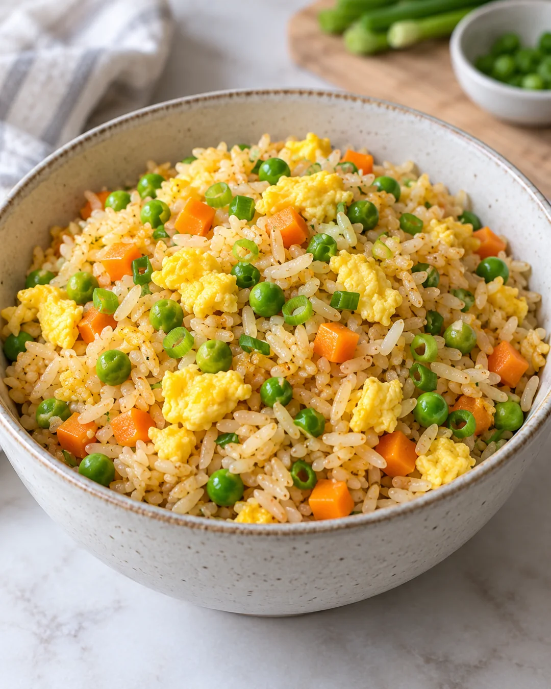 Egg fried rice with separated grains, cooked egg pieces, peas, carrot and scallions.