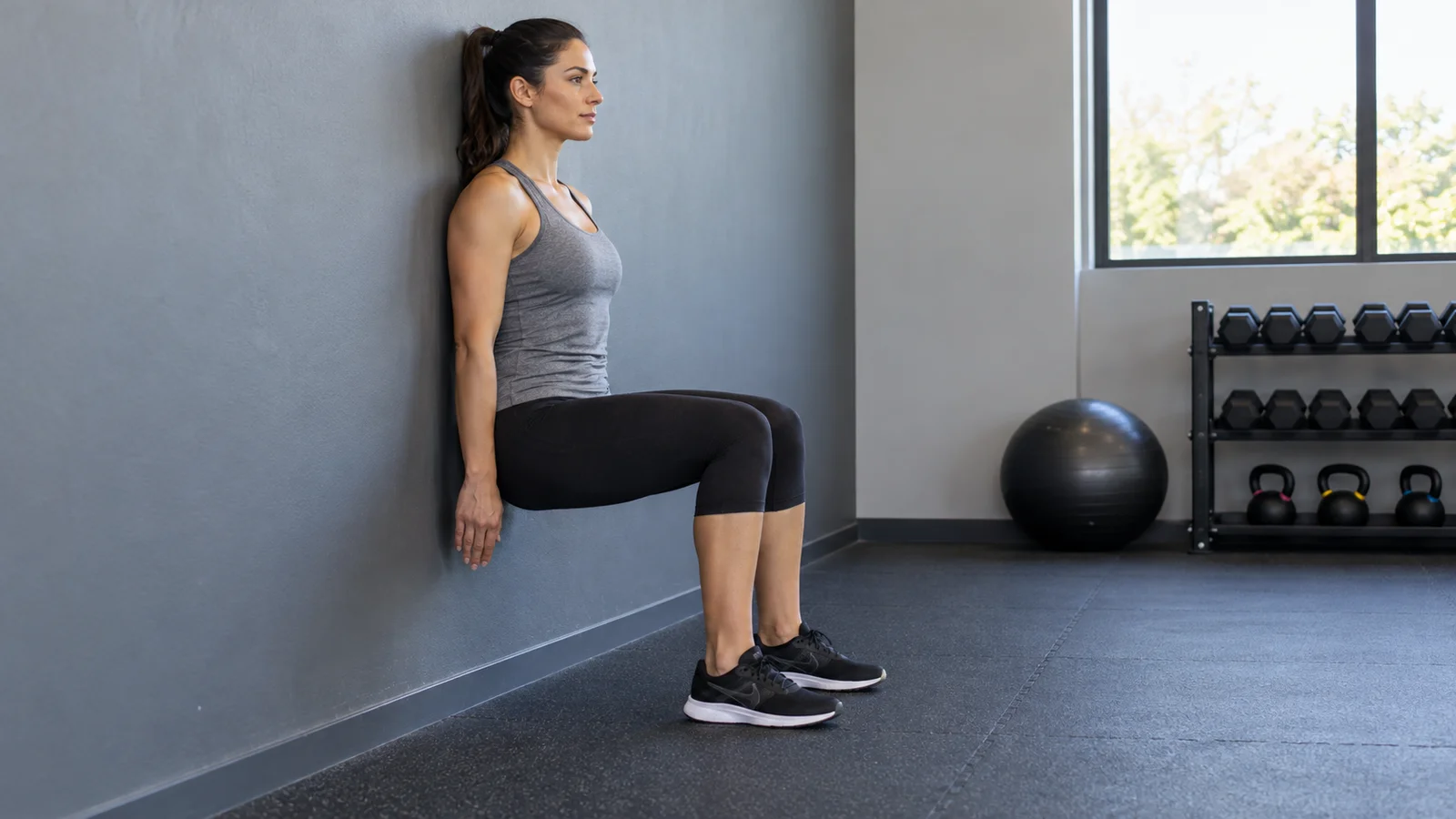 Woman holding a wall sit with her back against a wall and feet flat on the floor.